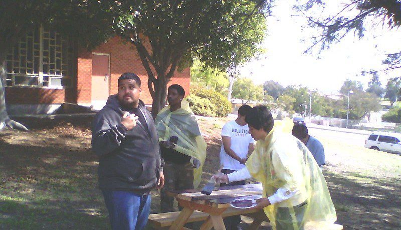Men painting picnic table outdoors.